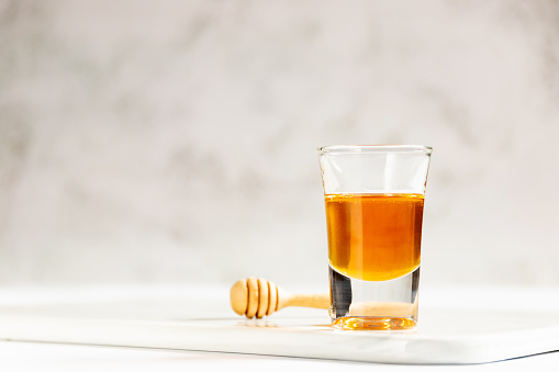Honey shot and wooden dipper on marble tray with light gray background