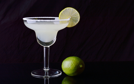Margarita cocktail and lime on black background.