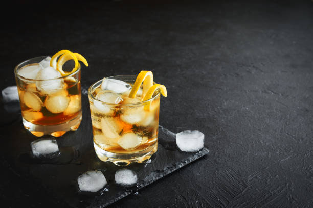 Whiskey or Rum on rocks with lemon twist on black stone background, top view, copy space.
