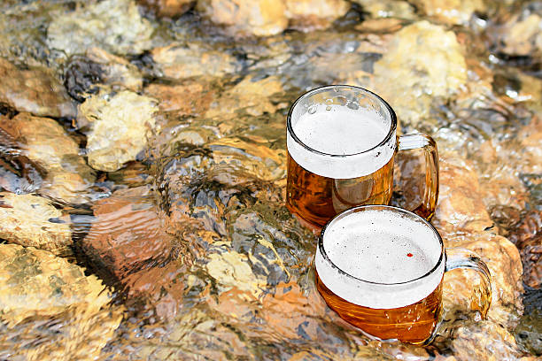 Two mug of excellent beer sparkles in the sun in a cool mountain stream